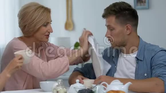 成熟的母亲照顾她的儿子把餐巾贴在他的脖子上妻子震惊了视频的预览图