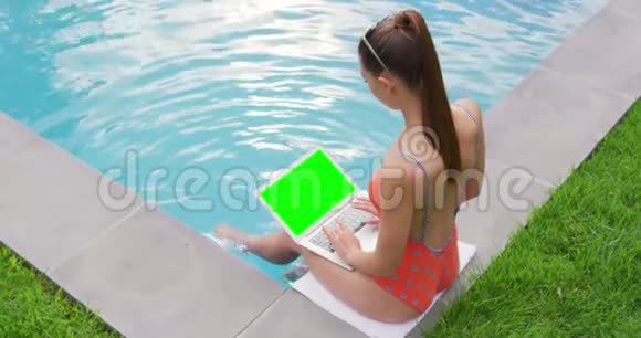 在后院游泳池附近使用笔记本电脑的女人视频的预览图