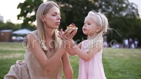 母亲和一个小女儿的肖像一起在城市公园野餐他们咬小蛋糕视频的预览图
