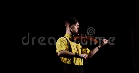 男职业小提琴手在黑色背景下拉小提琴在黑暗中正面观看视频的预览图