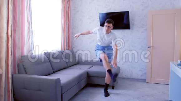 有趣的书呆子正在蹲着倾斜的腿用他的手触摸腿在家里锻炼生活视频的预览图