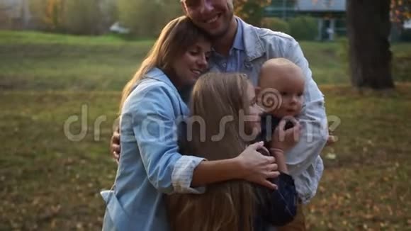 夫妻在秋天公园拥抱他们的两个孩子幸福的家庭散步城市公园的日落视频的预览图
