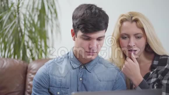 年轻夫妇坐在家里的笔记本电脑前一个黑发男人和金发女人检查邮箱的肖像视频的预览图