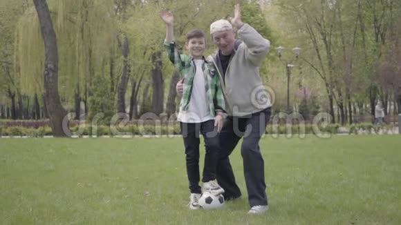 那个穿着格子衬衫的小男孩和积极的老人向公园里的摄像机挥手孙子视频的预览图