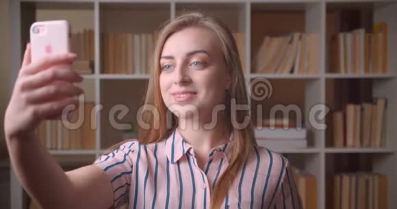 一位年轻漂亮的白种人女学生在大学图书馆打电话视频特写视频的预览图