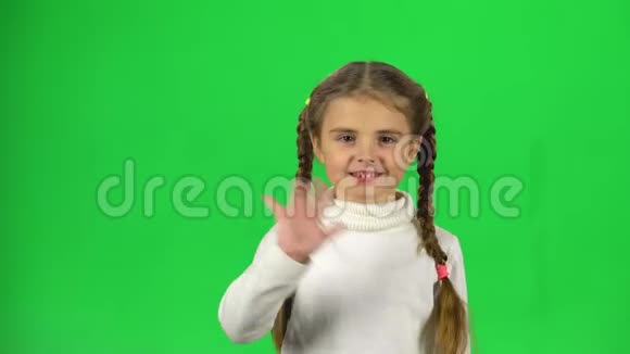 有两条辫子的女孩在挥手问好并邀请她来到绿色背景下视频的预览图