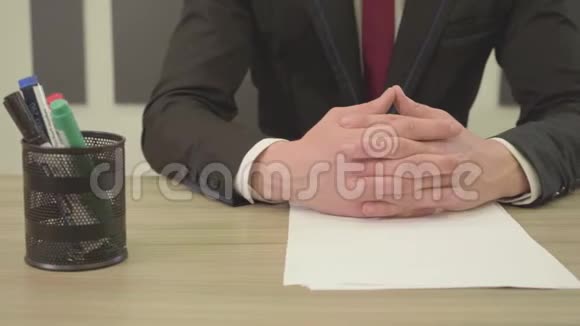 穿着西装的面目全非的人坐在桌子前交叉的手指放在空白的纸钢笔和眼镜前大人物视频的预览图