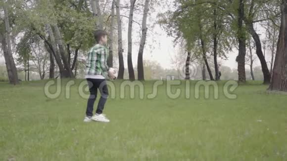 那个穿格子衬衫的小男孩在公园里踢足球那孩子用他的脚和它击球视频的预览图