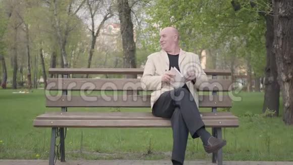 那个秃顶的成熟男人坐在公园的长凳上看书一个小男孩来找他爷爷带着视频的预览图