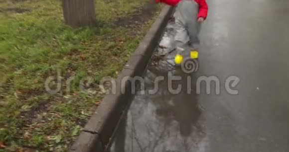 穿着黄色靴子穿过水坑的男孩视频的预览图