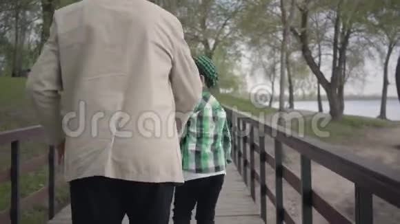 祖父和孙子在桥上的公园里散步孩子开始跑叫那个人加入他的行列这就是视频的预览图