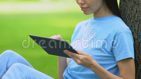 女性自由职业者在平板电脑上工作坐在公园的草地上远程访问视频的预览图