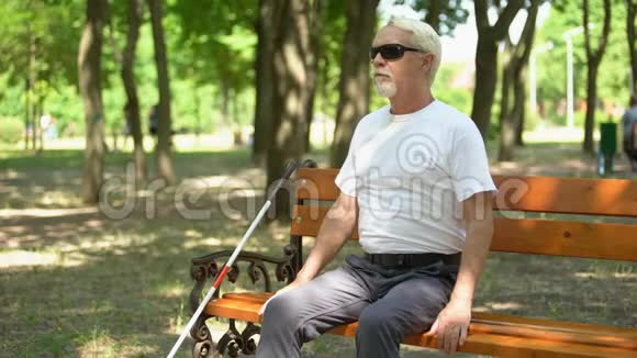老瞎子在长椅上找长拐杖在公园里独立行走休息视频的预览图