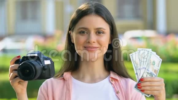 快乐的女摄影师拿着相机和钱爱好赚钱收入视频的预览图