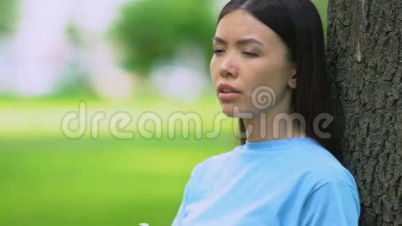 年轻女子坐在阳光明媚的公园里打喷嚏季节性过敏症状视频的预览图