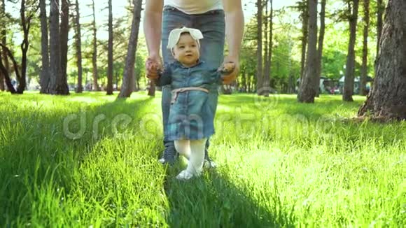 在阳光明媚的公园里蹒跚学步的女孩在草地上从父亲走到母亲的第一步视频的预览图