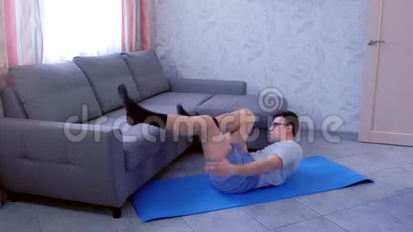 一个书呆子正躺在家里的垫子上做动态的仰卧起坐练习运动幽默概念视频的预览图