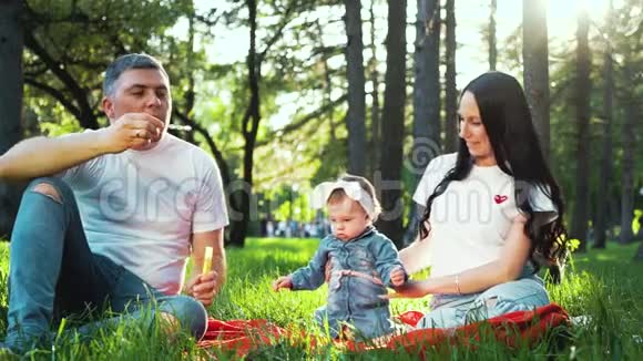 快乐的一家人和小女孩一起在夏天的公园里吹肥皂泡视频的预览图