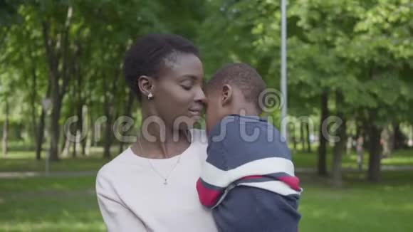 肖像漂亮的非洲裔美国妇女抱着她的儿子在她的绿色公园近距离可爱的孩子花时间视频的预览图