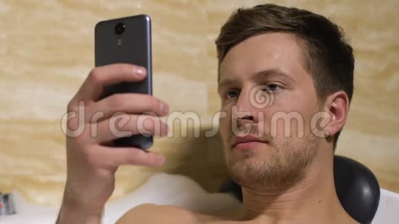 帅哥滚动智能手机躺在浴室社交网络交流视频的预览图