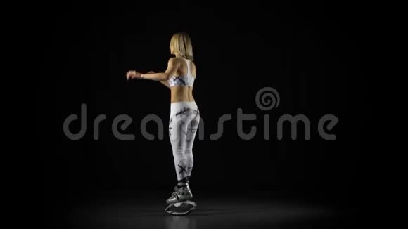运动女孩穿着kangoo鞋在摄影棚黑色背景的烟雾中的聚光灯中跳跃视频的预览图