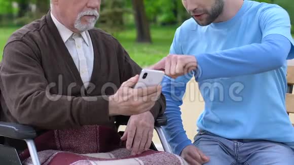 男性志愿者教坐轮椅的老人如何使用智能手机护理视频的预览图
