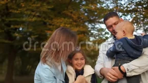 秋天公园有两个孩子的幸福家庭年轻夫妇蹒跚学步的孩子和十几岁的女孩拥抱在秋天的公园幸福的家庭视频的预览图