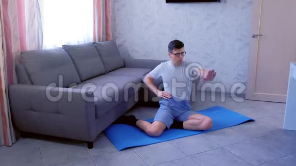 有趣的书呆子在家里坐在垫子上做手操体育幽默概念视频的预览图
