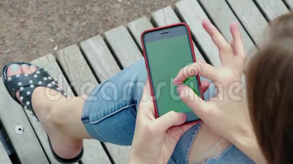 公园里年轻漂亮的女孩手里拿着一个绿色屏幕的黑色智能手机女人手拿电话视频的预览图
