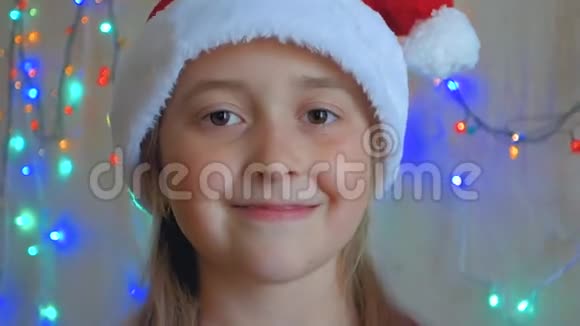 小女孩戴着圣诞老人的帽子背景是闪烁的花环少女可爱的微笑背景花环视频的预览图