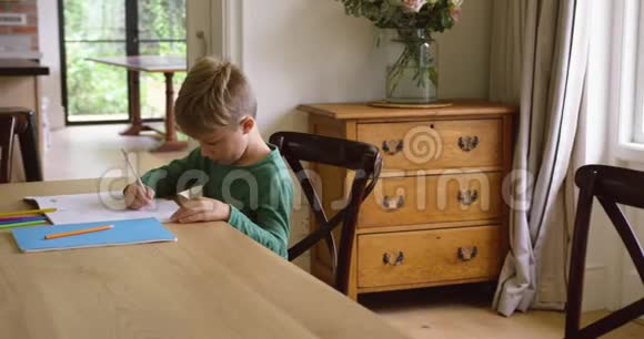 可爱的男孩在舒适的家里的餐桌上做作业视频的预览图