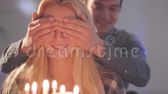 年轻人遮住金发美女的眼睛然后让她看到插满蜡烛的蛋糕女人过生日视频的预览图