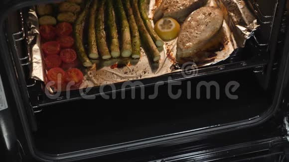 烤三文鱼牛排和蔬菜在电烤箱里准备的煮熟的鱼和西红柿健康饮食女人得到了视频的预览图