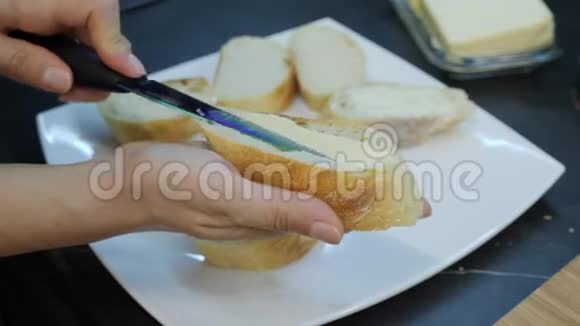 女人把黄油涂在白面包上双手合拢涂抹面包上的黄油用玛格丽特做罐头家庭烹饪视频的预览图