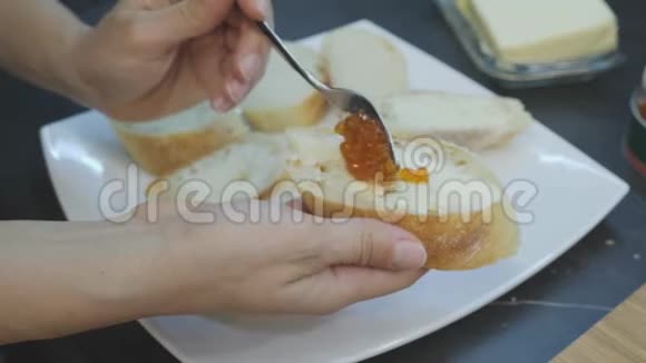 厨师把红色鱼子酱涂在罐头上手拿红鱼子酱加黄油在面包上用roe做三明治的过程家庭烹饪视频的预览图