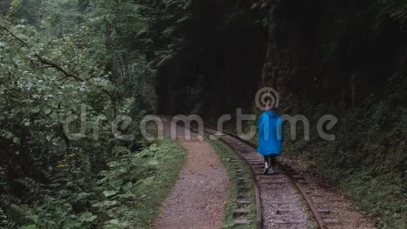 穿蓝色雨衣的女孩沿着旧铁轨走视频的预览图