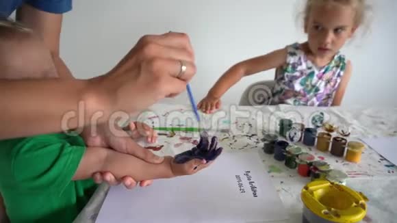 女儿看着妈妈和小儿子在纸上用水粉做掌纹视频的预览图