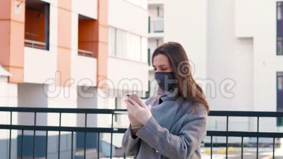 城市街道上的年轻女孩戴着黑色无菌医疗面罩用餐巾纸擦拭手机女人用电话视频的预览图