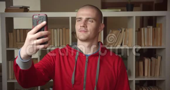 在大学图书馆里一位年轻迷人的白种人男学生在室内通过电话自拍的特写照片视频的预览图
