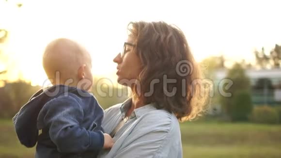 年轻的母亲把她两岁的孩子抱在怀里在日落时分柯利和她的儿子在秋天公园散步视频的预览图