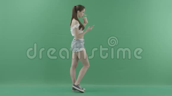 女人一边喝鸡尾酒一边在智能手机上发短信一边看着一个绿色背景的人视频的预览图