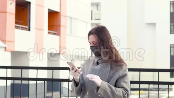 城市街道上的年轻女孩戴着黑色无菌医疗面罩女人用电话搜索有关nCov的新闻视频的预览图