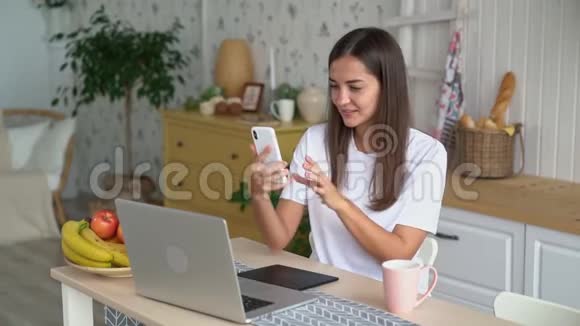 女人微笑在手机上自拍在家里用笔记本电脑工作慢动作视频的预览图