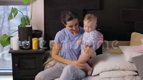 快乐苗条的妈妈和一个一岁的儿子在明亮的卧室里玩得很开心视频的预览图
