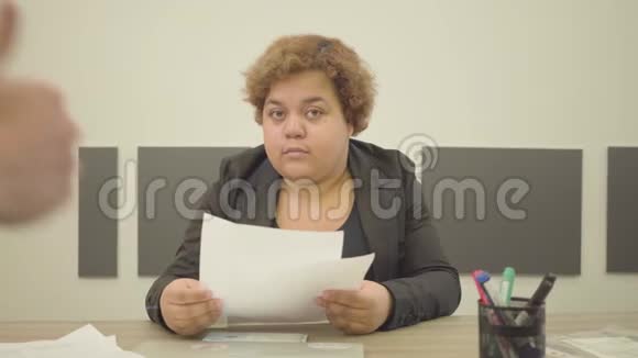 穿着正式服装的胖女人坐在办公室的桌子旁做文书工作一只手伸出大拇指视频的预览图