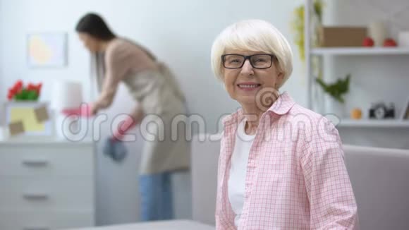 微笑的老妇人看着相机管家在房间里擦拭灰尘打扫卫生视频的预览图