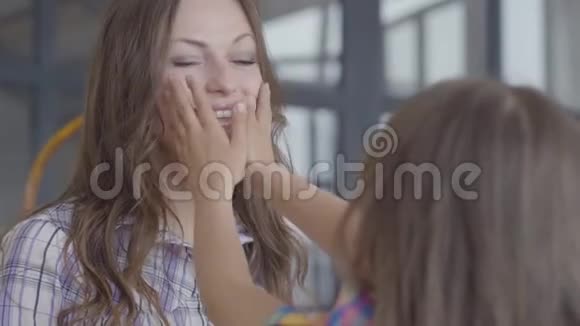 年轻的母亲和可爱的女孩一起在厨房关门孩子用她的小摸着妈妈的脸拉着她的脸视频的预览图