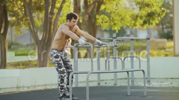 年轻的运动赤膊男子在娱乐公园的双杠上做运动视频的预览图