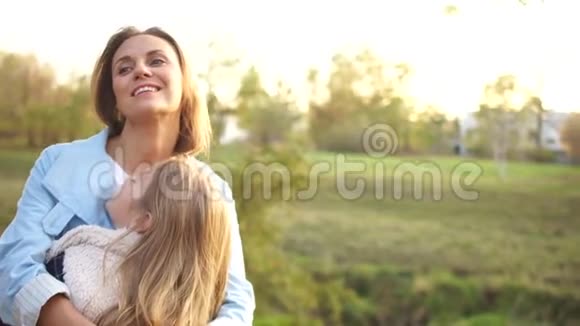 幸福的一家人妈妈和女儿正抱着在城市秋天公园迎着夕阳女孩们开心地笑着视频的预览图