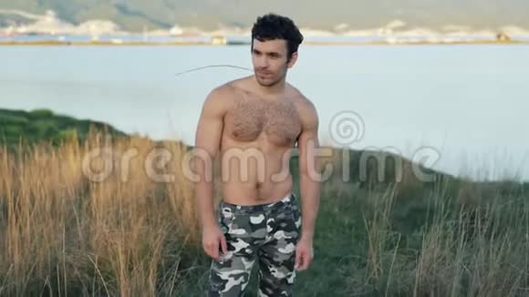 英俊的年轻肌肉男站在田野里背景是山和海视频的预览图